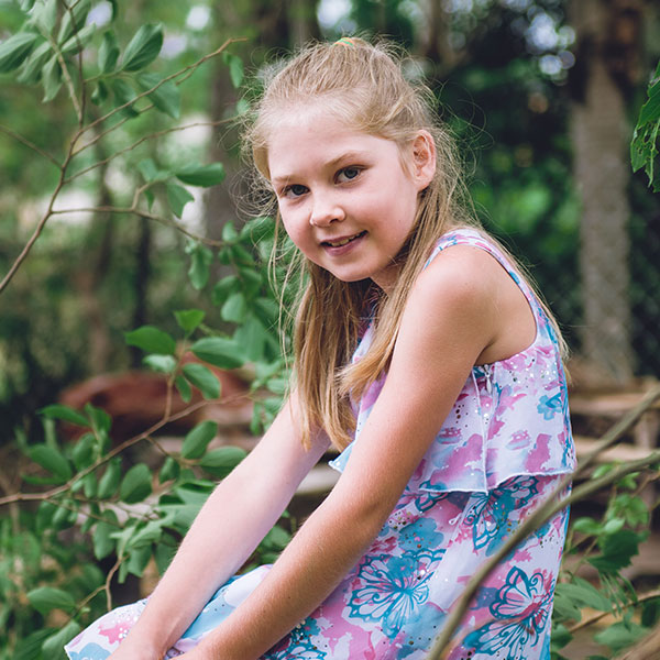 young blonde-haired girl sitting in a forest smiling into the camera