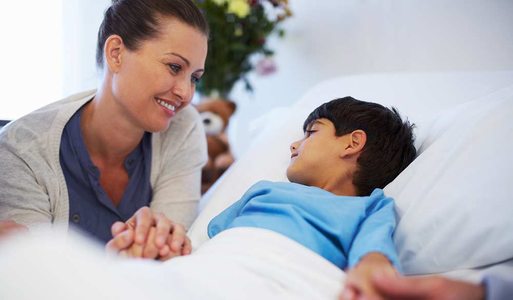 young boy laying in hospital bed being comforted by his mother