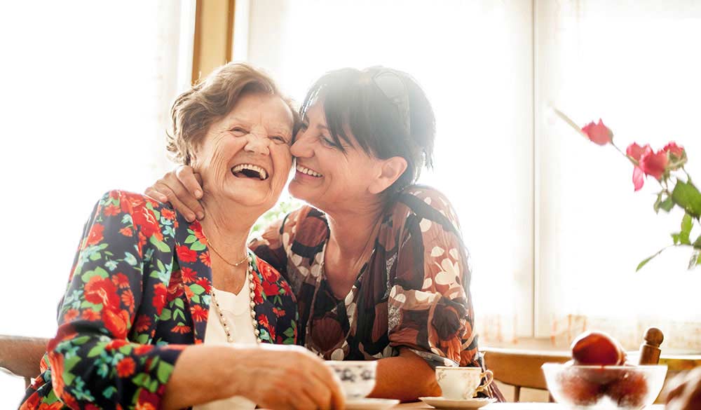 elderly mother laughing drinking coffee with daughter