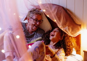 Grandmother and granddaughter laughing in bed surrounded by fairy lights