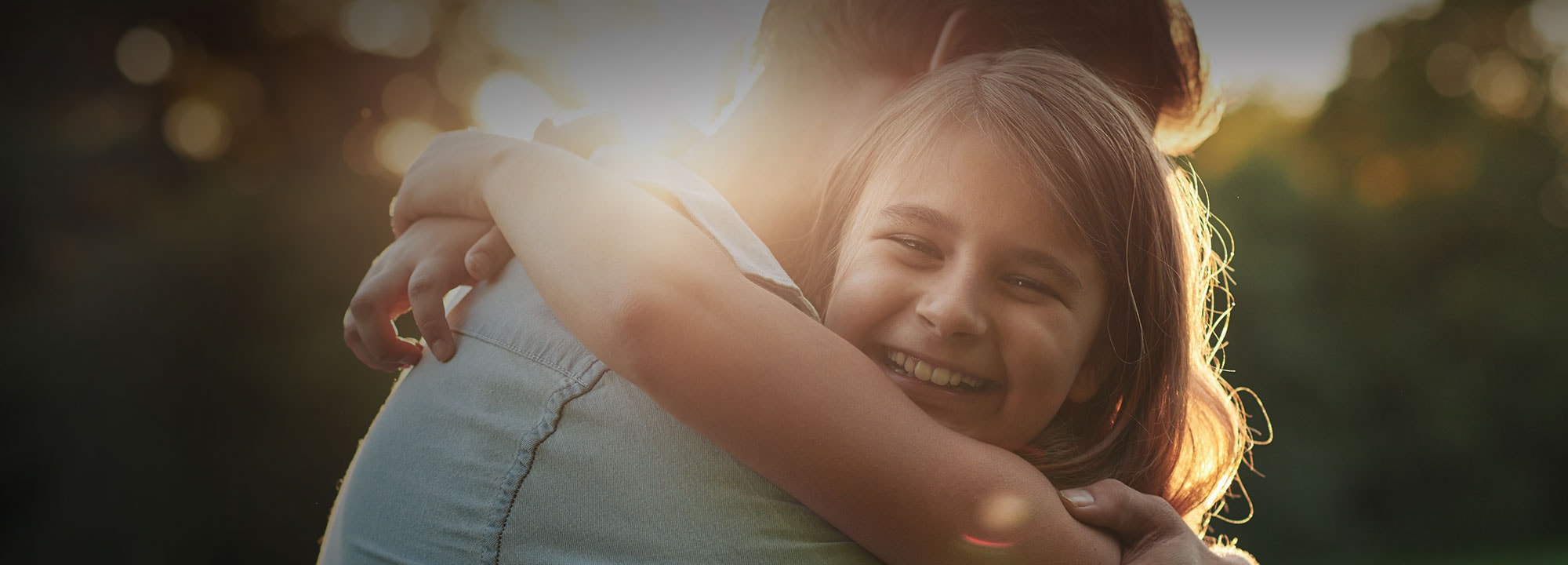 A father hugging his daughter outlined by the sun