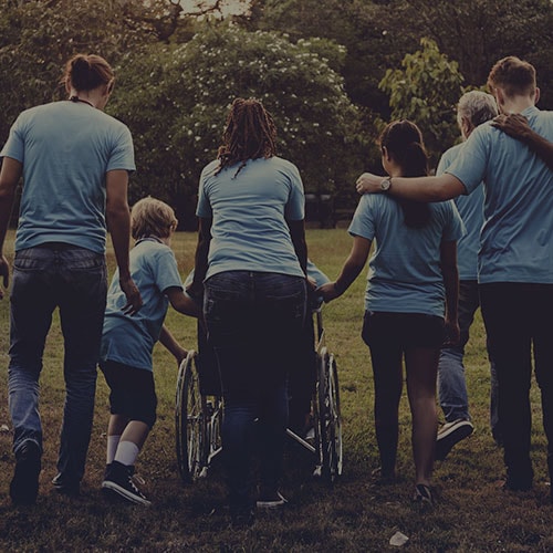 multiple volunteers embracing outdoors while helping a disabled client