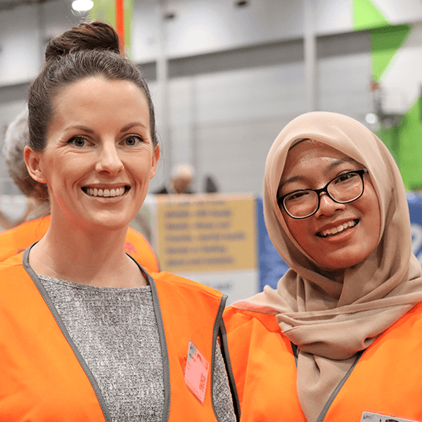 Two women smiling at the camera, with orange vests on