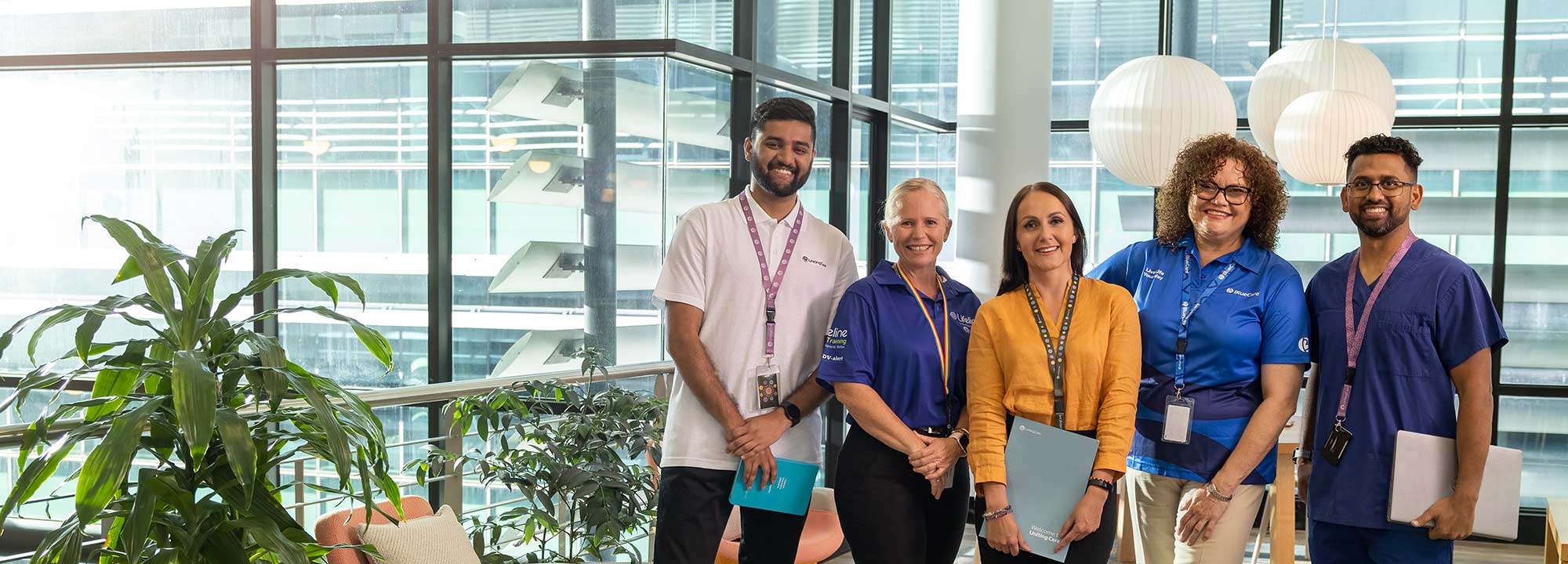 Five UnitingCare staff members, from across the organisation stand in head office, with city buildings visible through the glass walls.