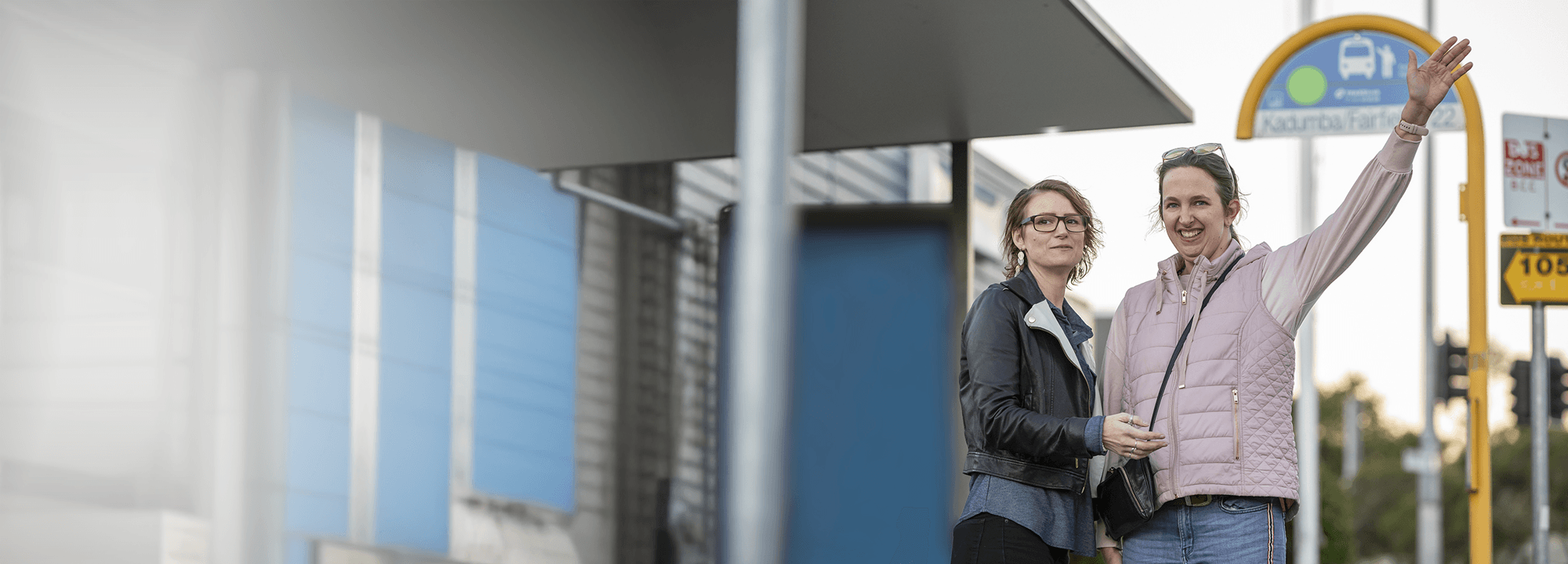 two women hailing a bus at a bus stop.