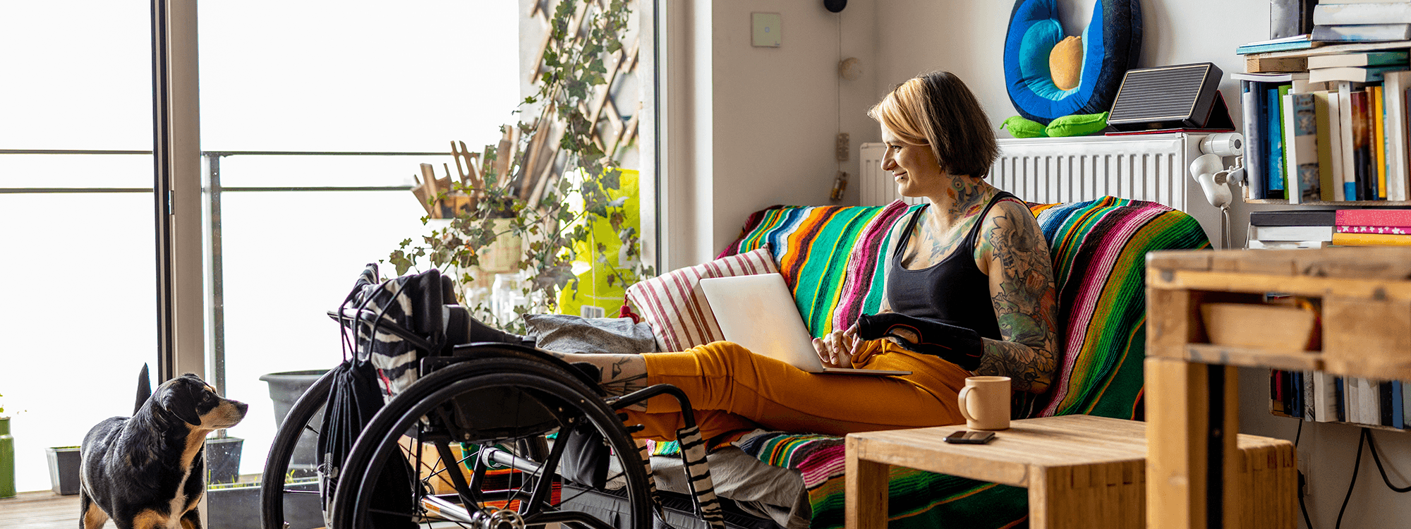 a woman on her laptop with her legs up on her wheelchair smiling at her dog
