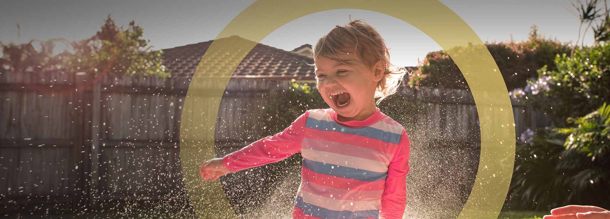 young child wearing a bright rash vest splashing water and smiling outdoors