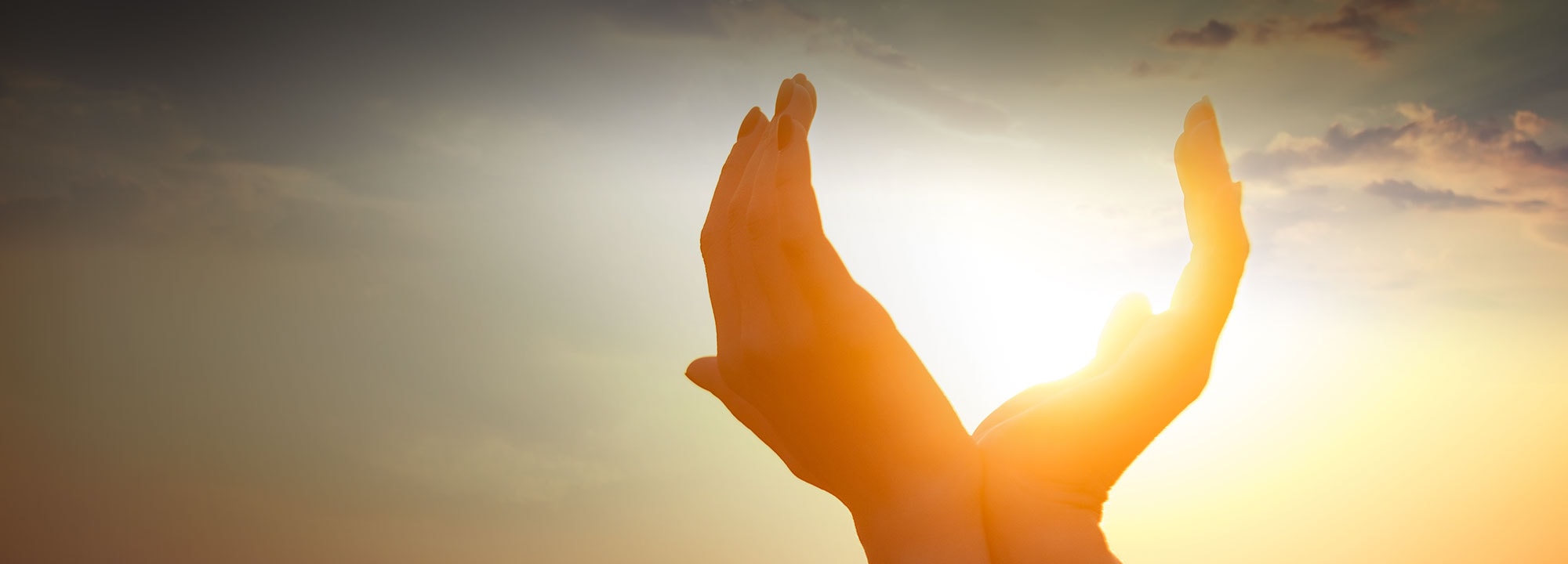 two hands cupping the sunlight as it radiates from a vibrant sunset taking place in the background