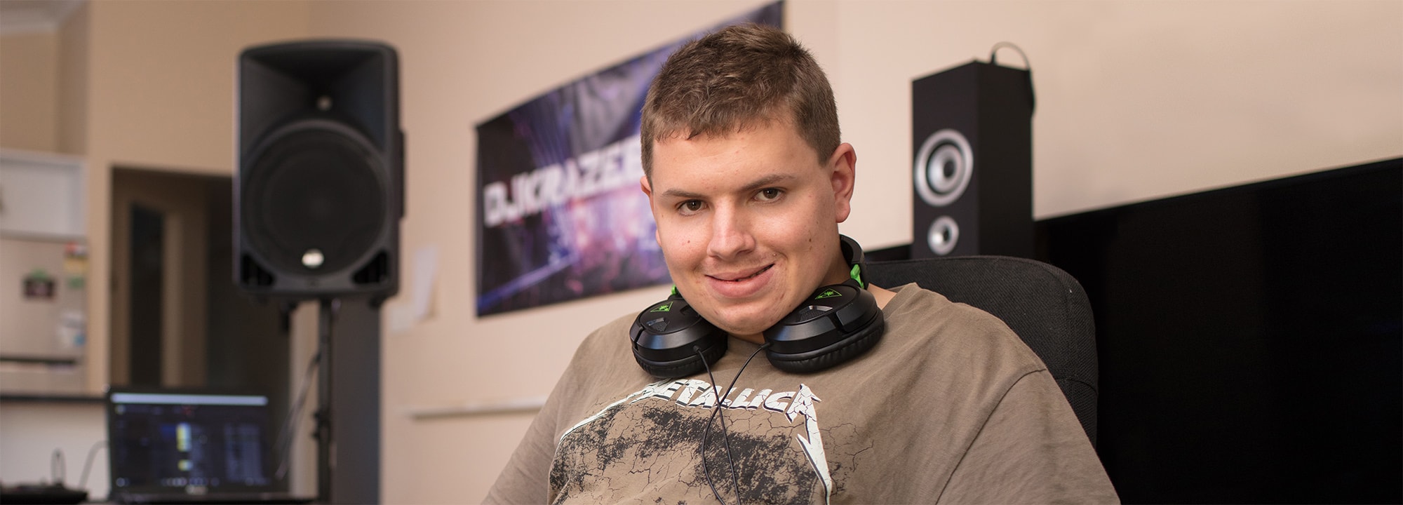a young man in a metallica t-shirt sitting in a music studio with headphones around his neck