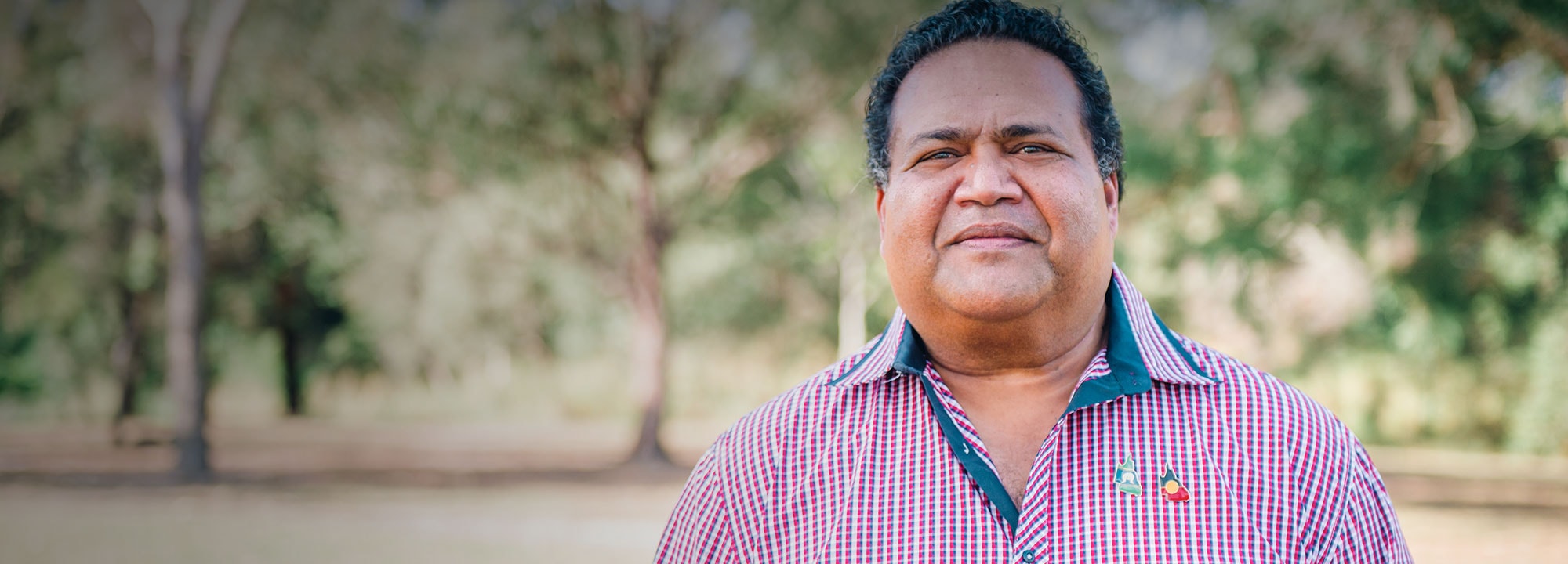 an indigenous man in a pink button up standing outdoors