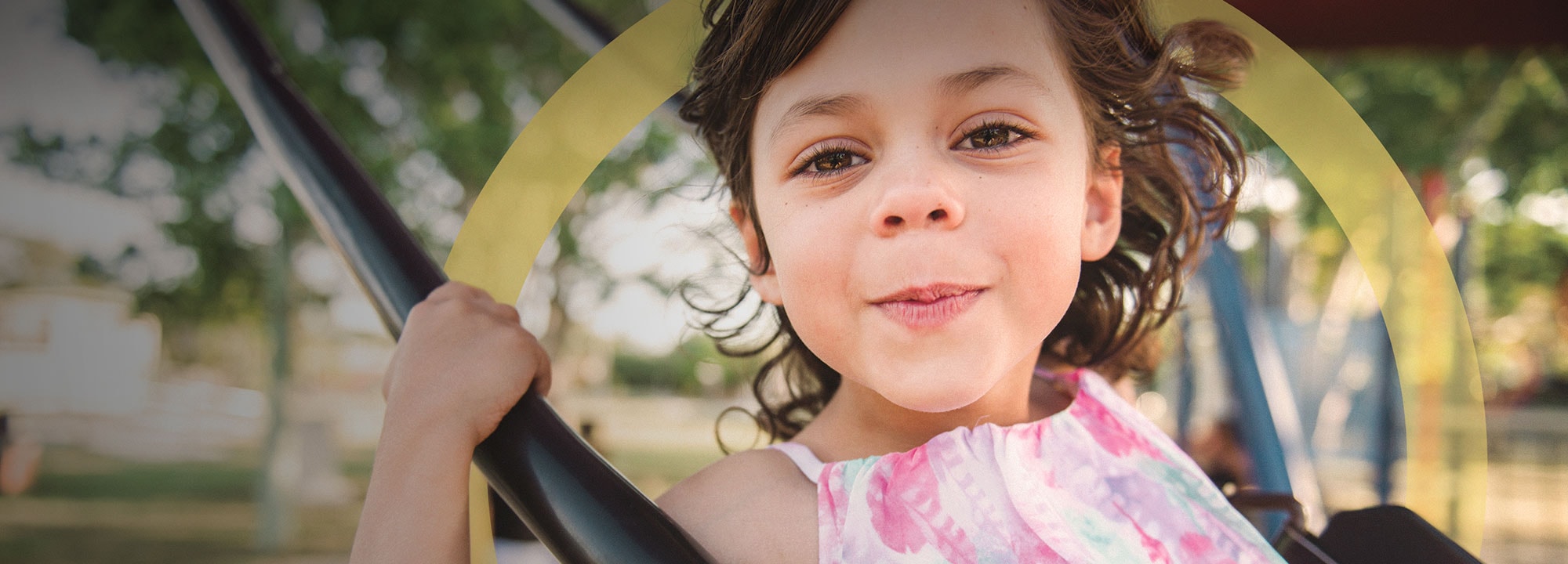 a young brown-haired girl smiling while playing on a swing