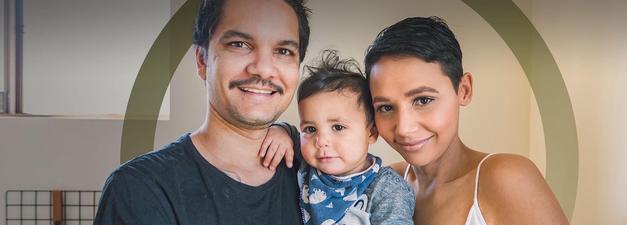 a man and woman smiling indoors while the man holds a child