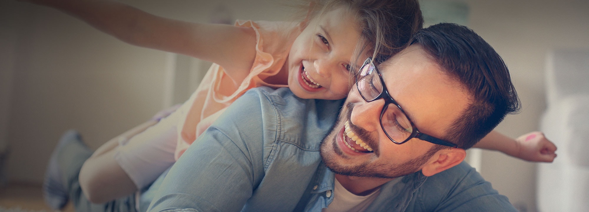 A laughing young girl leans on a laughing man wearing glasses.