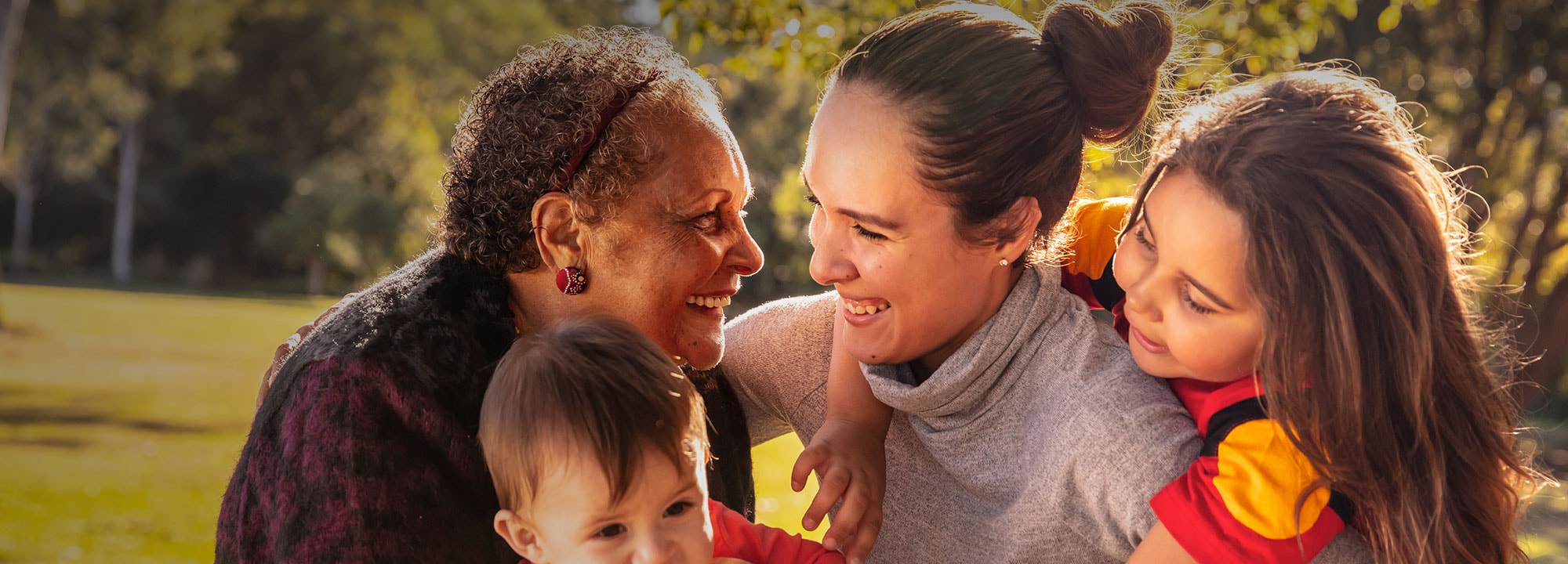 A smiling older lady and younger woman play with two children in a park.