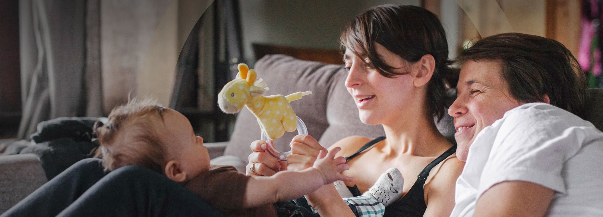 a young mother and father sitting on a couch playing with their infant child