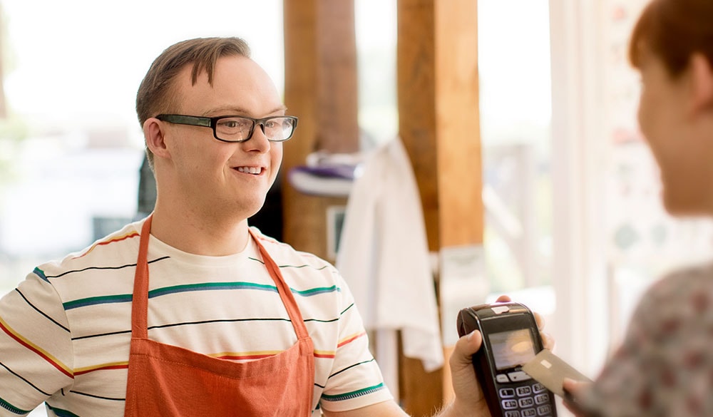 young disabled man at work smiling and offering a customer an eftpos machine for payment