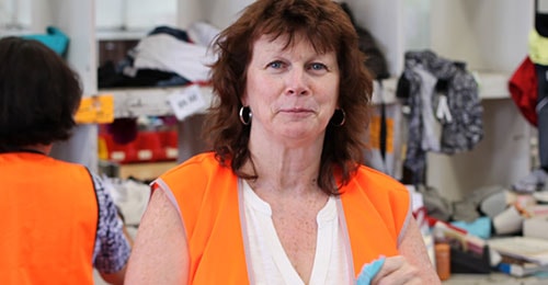 female volunteer wearing a bright orange vest working in a clothing donation facility