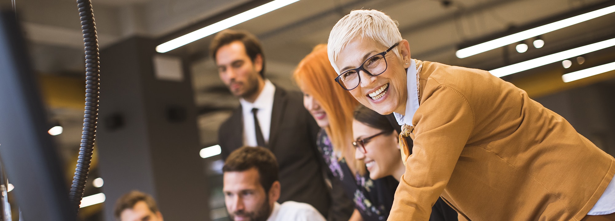A lady in a corporate office surrounded by colleagues smiling at camera
