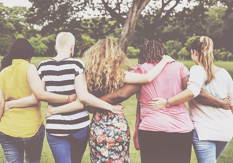 multi cultural group of woman embracing each other as they walk away