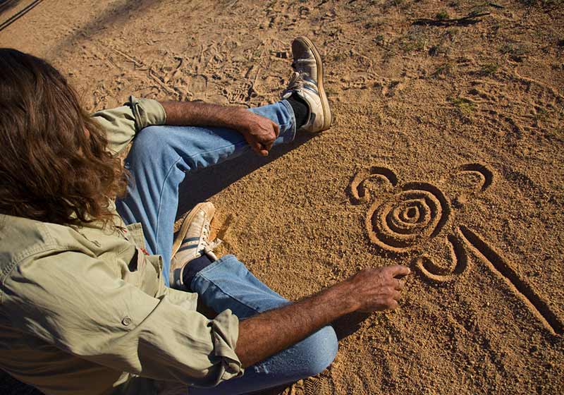 indigenous man drawing in sand in hollingsworth