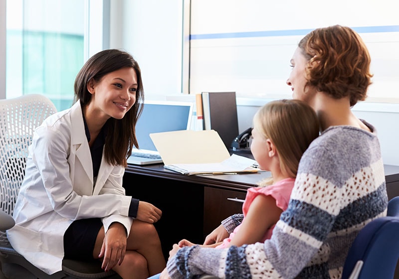 brunette woman doctor speaks to short red headed mother and child