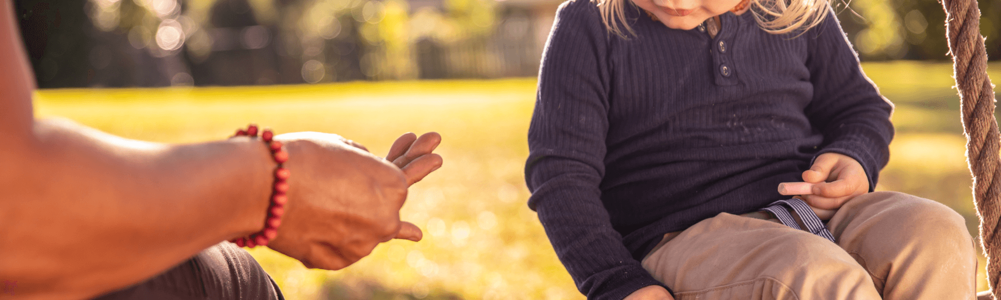 An unidentified adult and a child sit on a park bench.