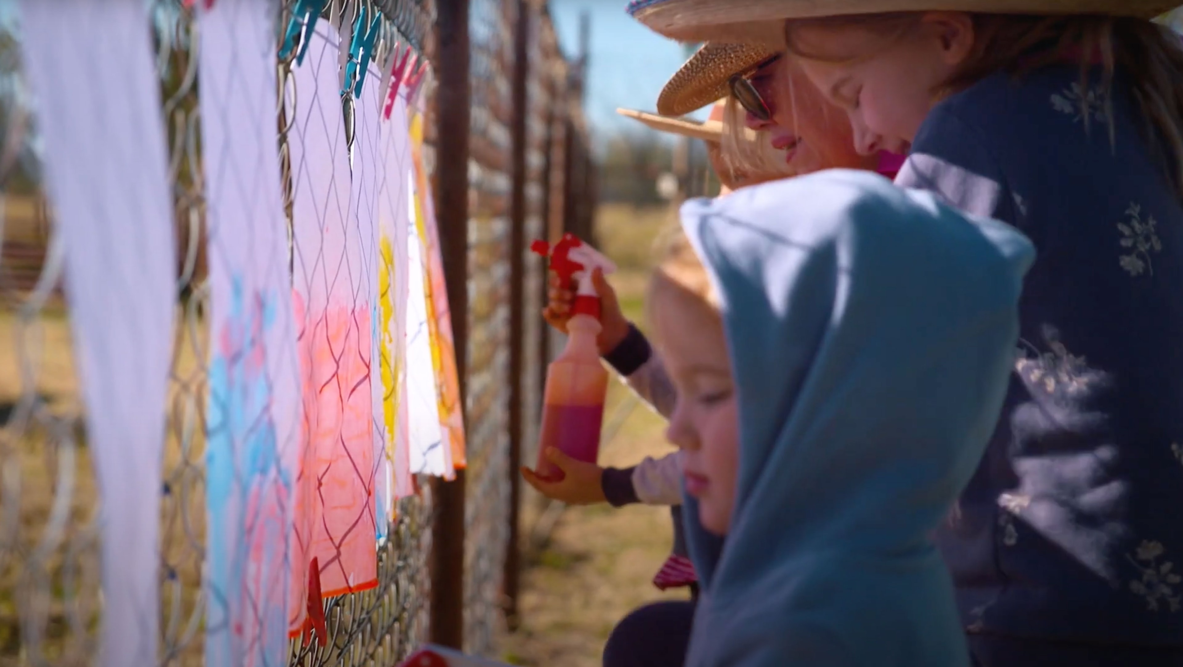 A family hanging up art on a wire fence outside