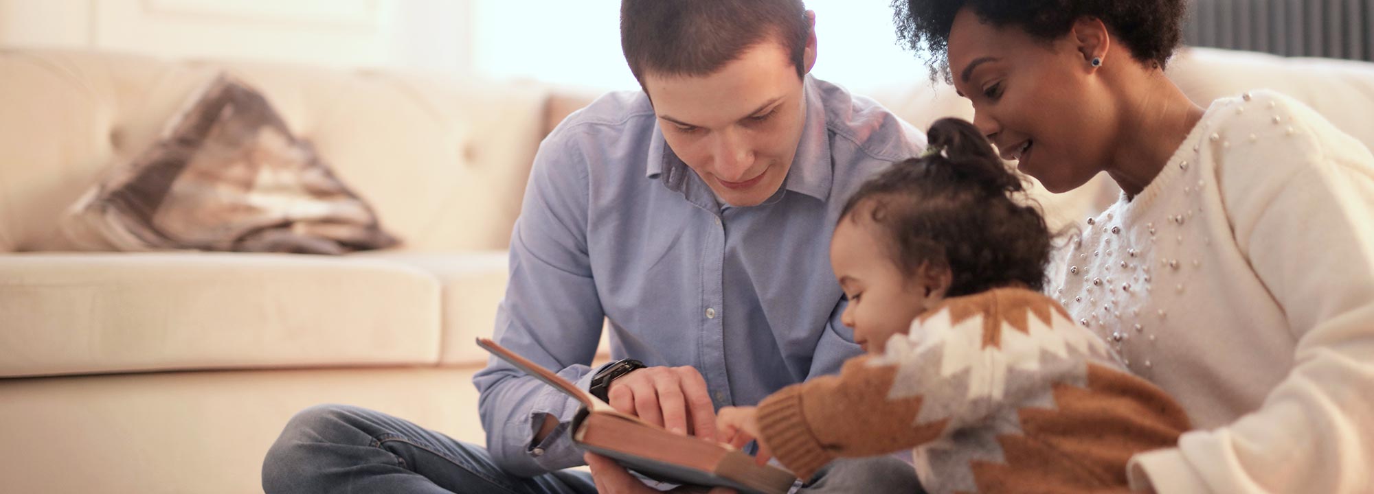 A multicultural family reading a book together in a living room