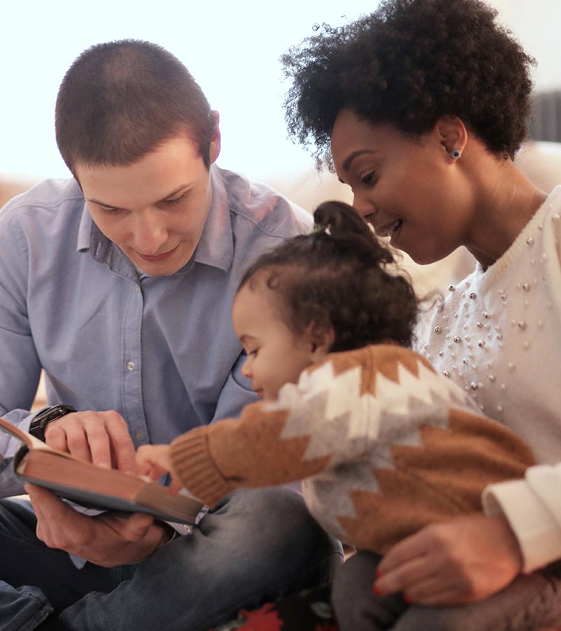 A multicultural family reading a book together in a living room