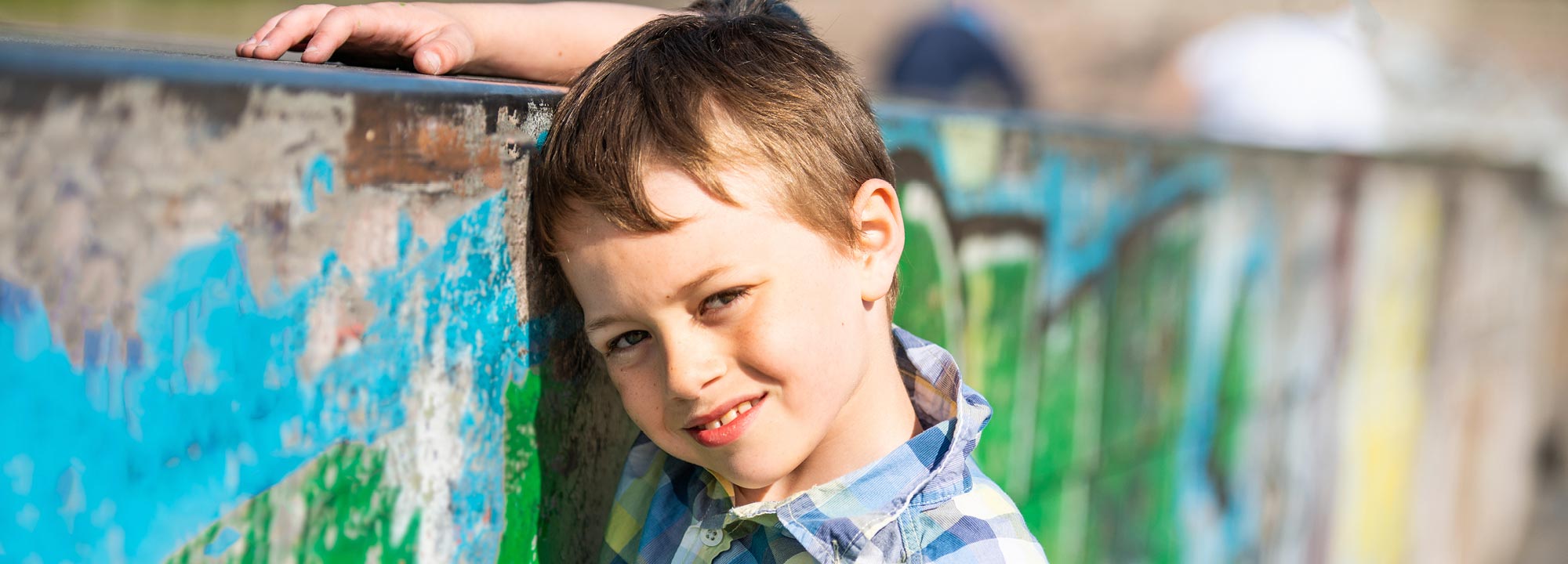 A young boy rests his head against a graffiti-covered wall.