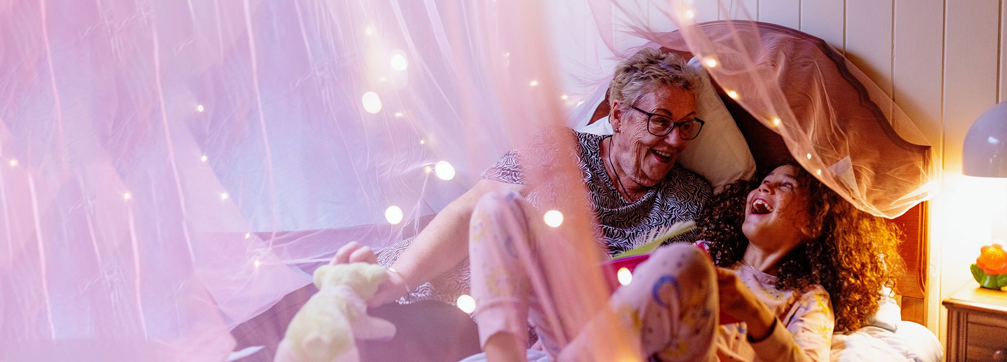 Grandmother and granddaughter laughing in bed surrounded by fairy lights