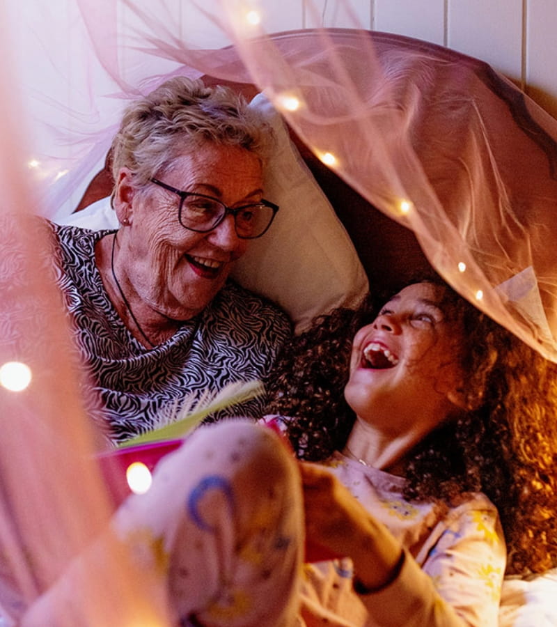 Grandmother and granddaughter laughing in bed surrounded by fairy lights